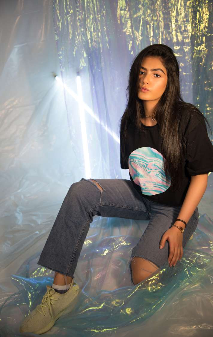 A girl wearing black round neck short sleeve T-shirt paired with grey torn denim and shoes is sitting on plastic.