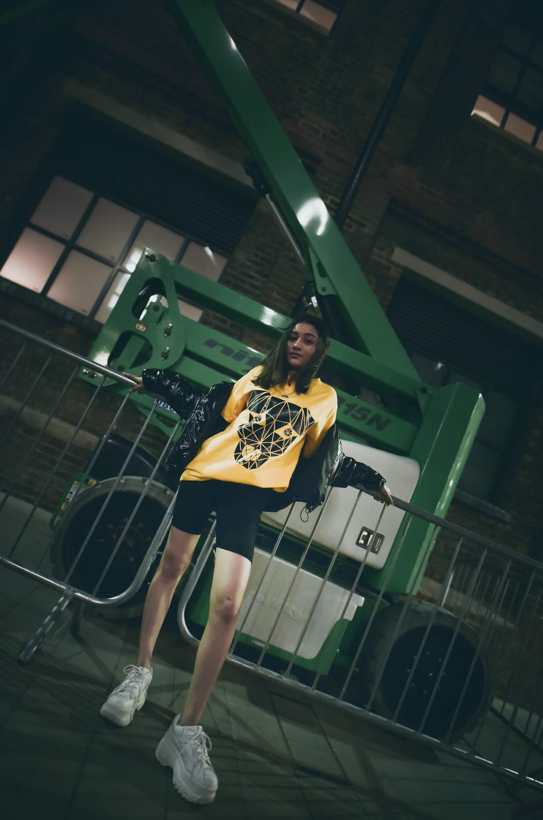 A girl wearing yellow round neck short sleeve regular fit T-shirt with dog printed on it is paired with black shorts and shoes is standing holding a grill.