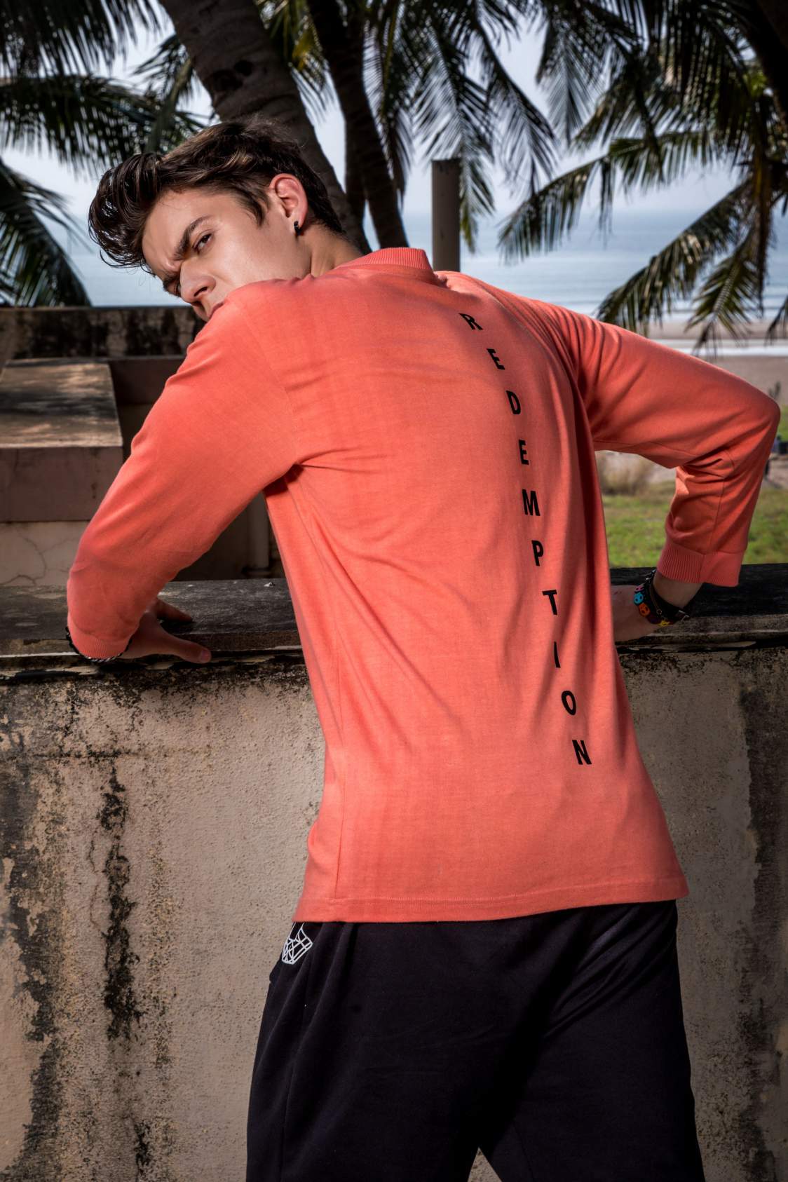 Close up of a boy Wearing pink full sleeved round neck T-shirt paired with black track pant is standing leaning on a wall