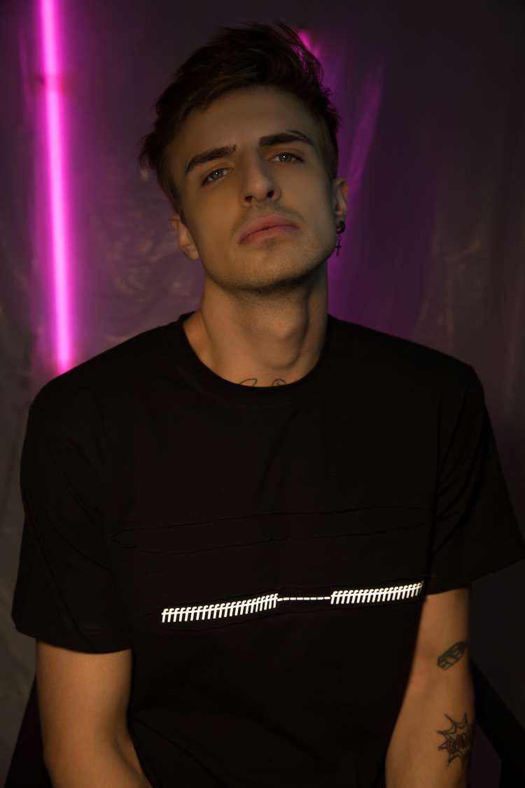 A Boy wearing black regular fit short sleeve round neck T-shirt with a lots of f printed and ripped in the center with a purple light in the background.